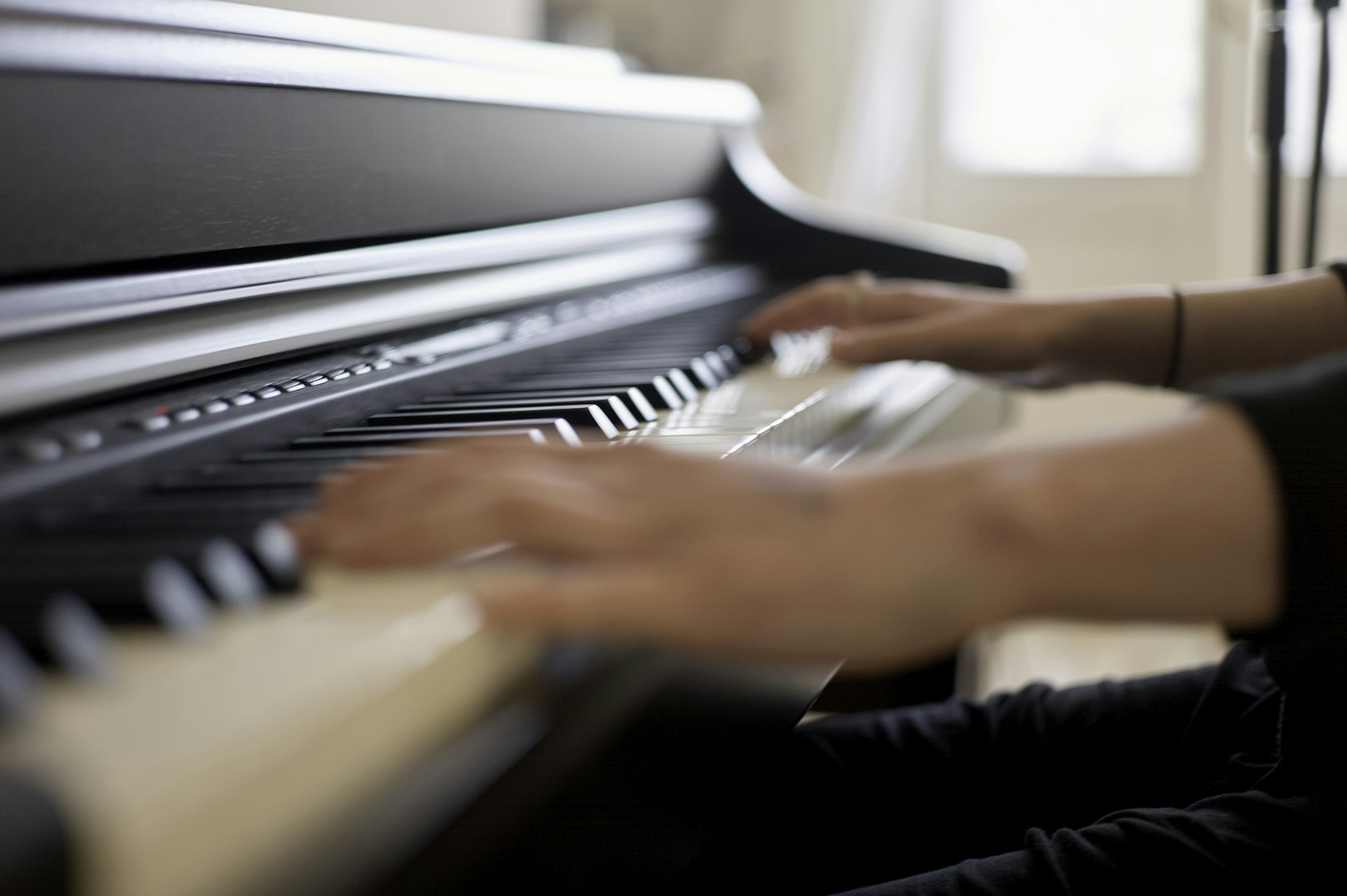 A person is playing a piano, focusing on their hands moving across the black and white keys.